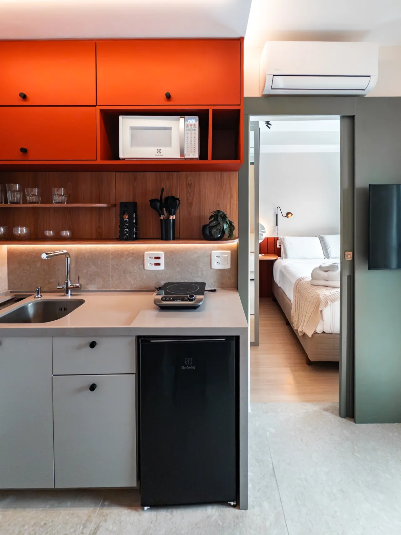 Cozinha compacta com pia, cooktop e geladeira, com vista para o quarto