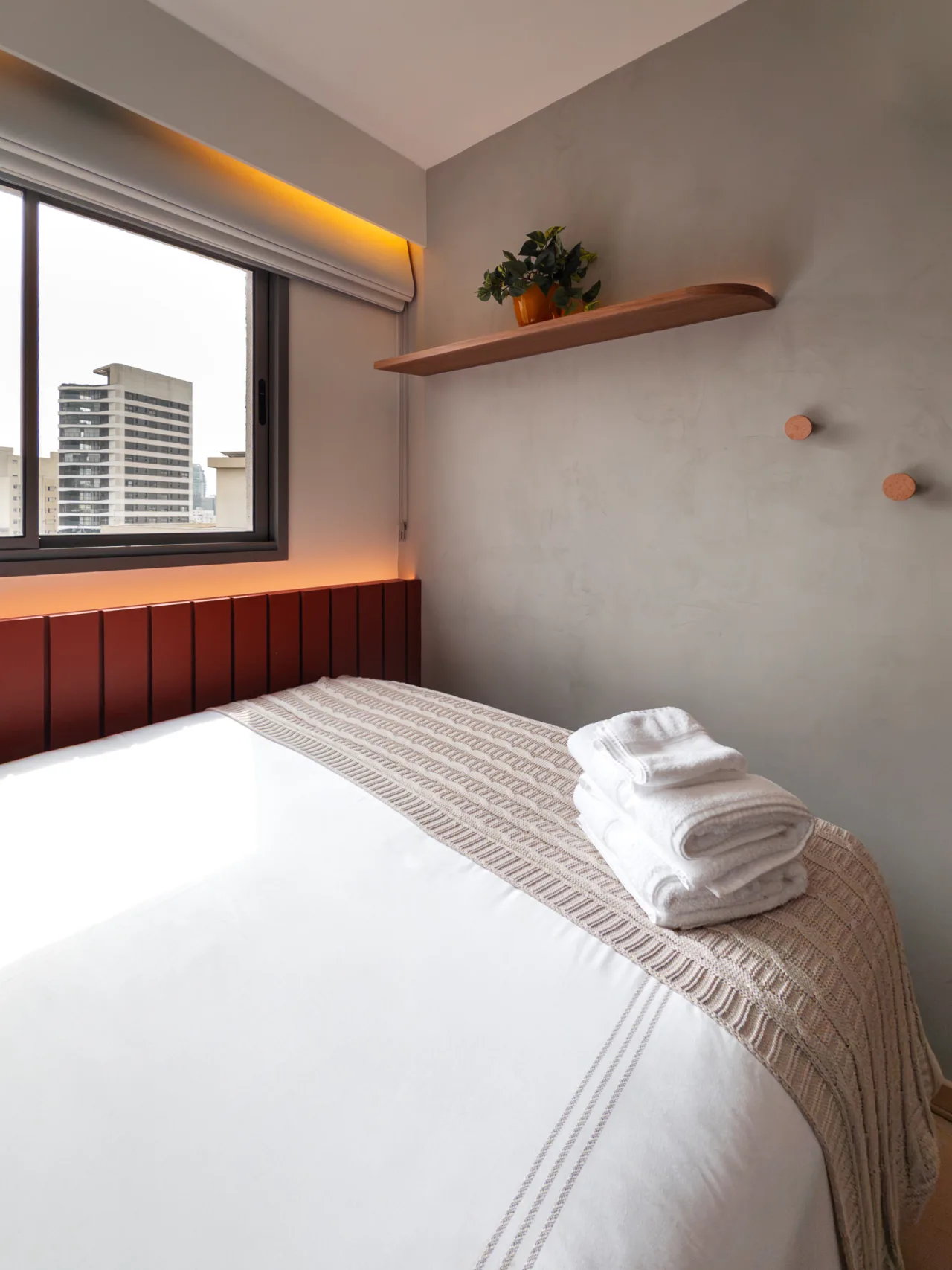 Quarto com cabeceira estofada, janela ampla e enxoval branco