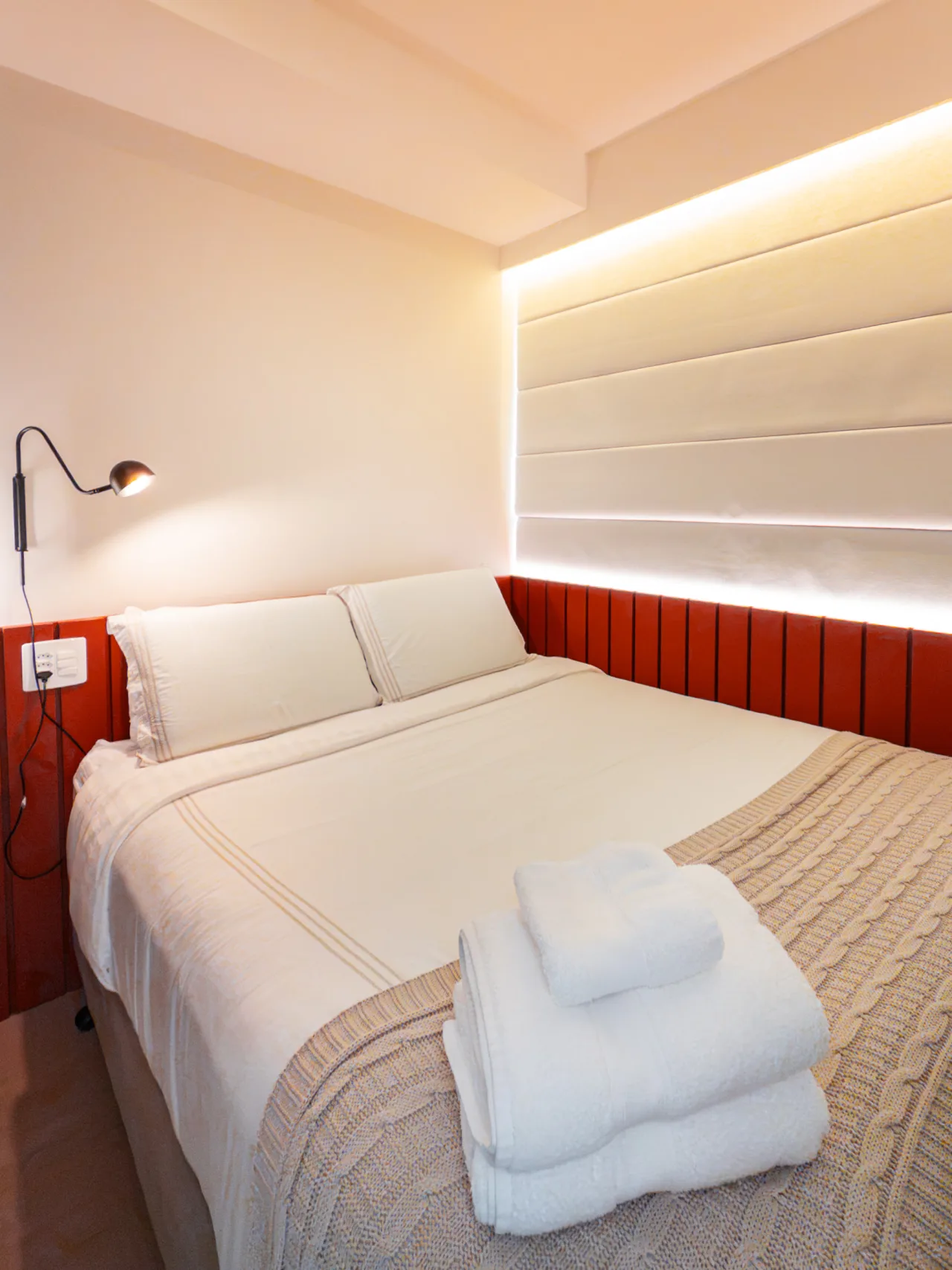 Quarto com cama de casal, cabeceira ripada e iluminação embutida