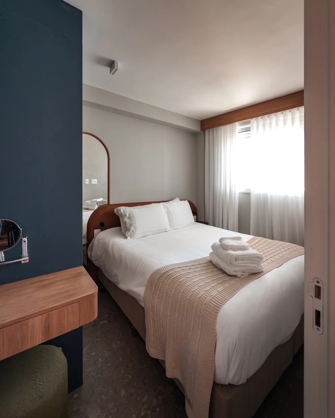 Quarto com cama de casal, cabeceira em madeira e cortina translúcida