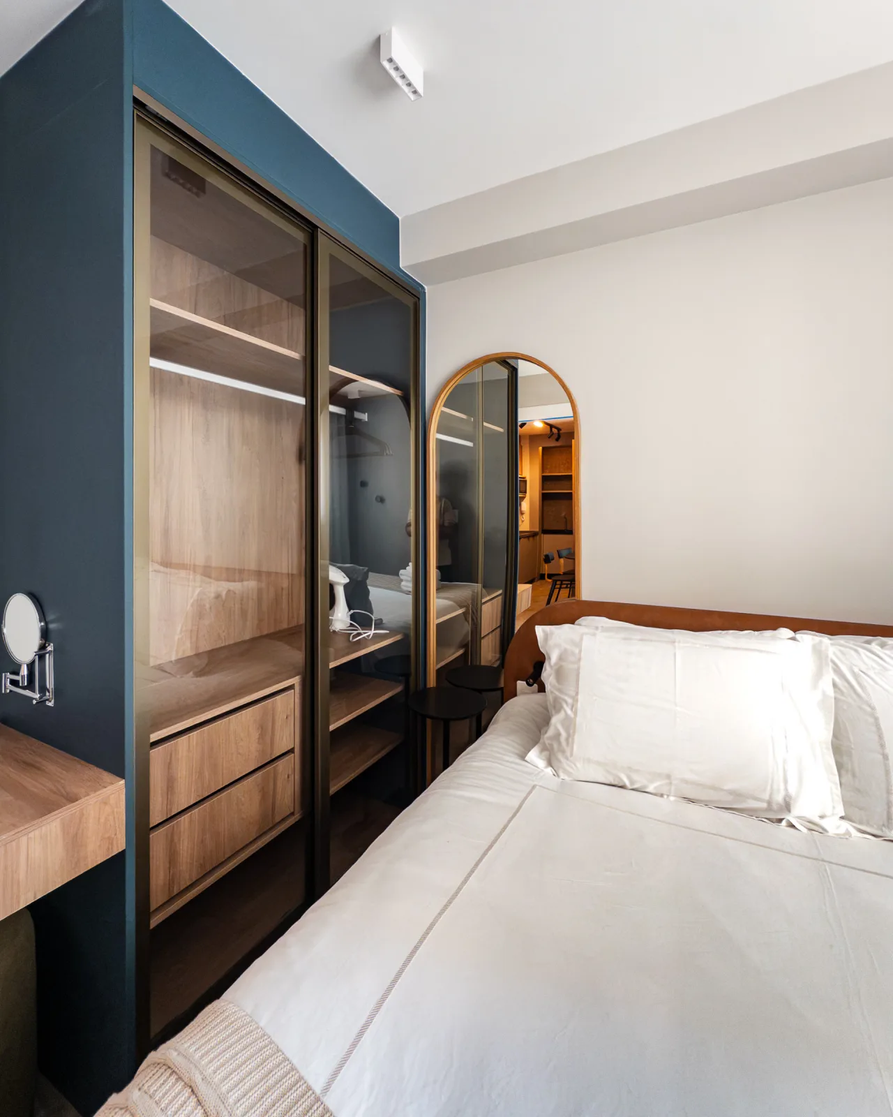 Quarto com closet envidraçado azul petróleo e espelho de moldura arqueada